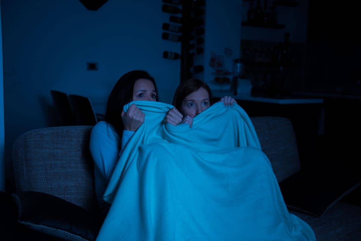 Deux personnes se cachent sous une couverture effrayées.