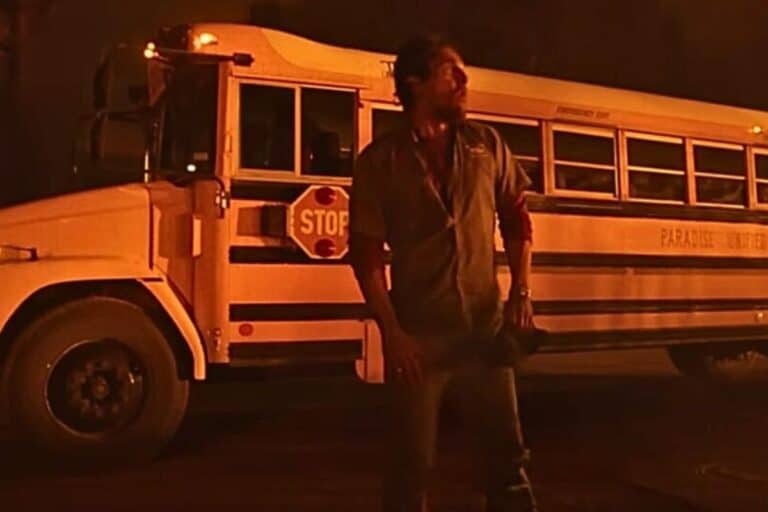 Homme debout devant un bus scolaire la nuit.