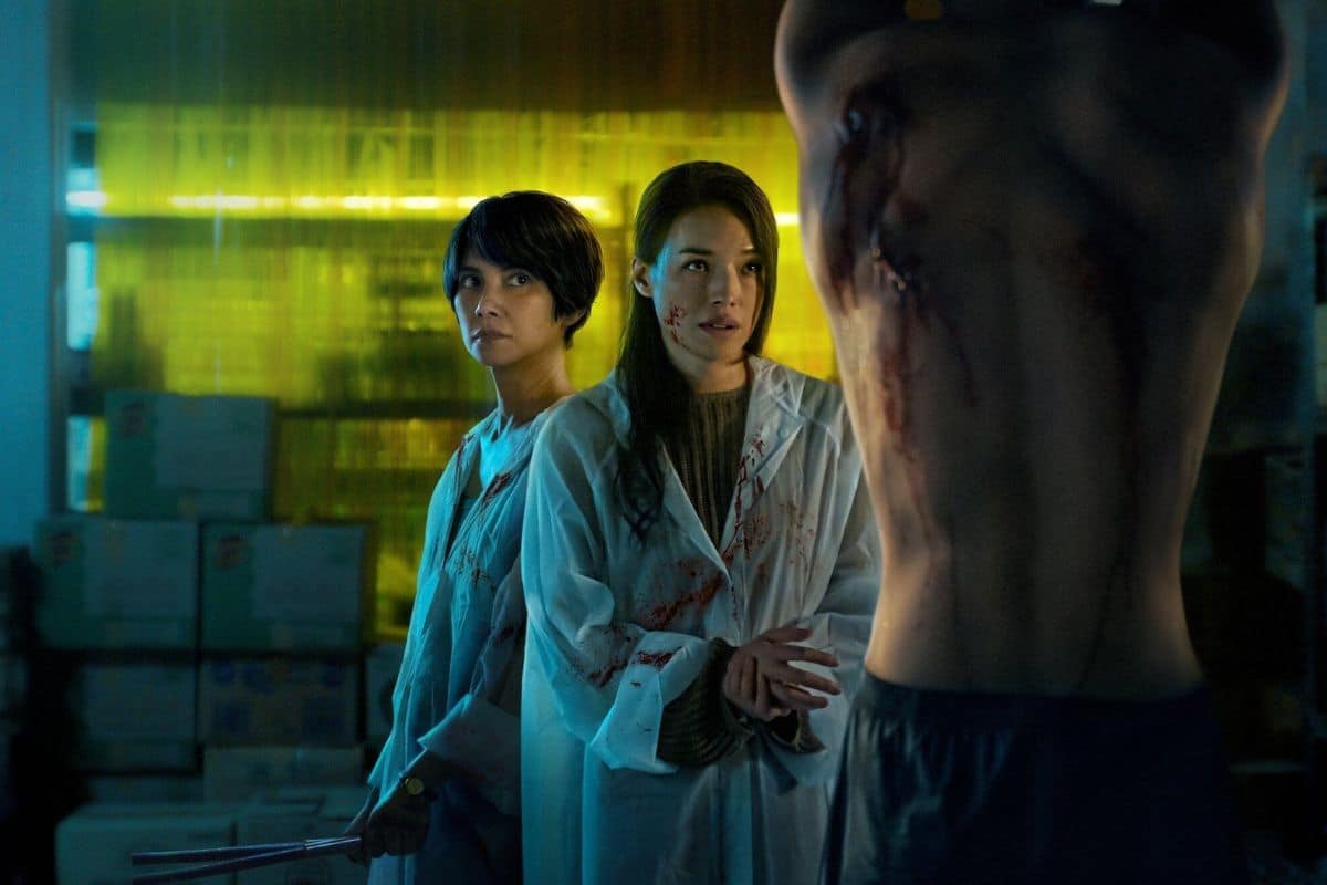 Deux femmes en blouse près d'un torse ensanglanté.