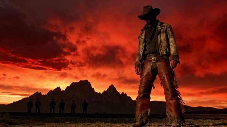 Cowboy silhouette devant coucher de soleil rougeoyant.