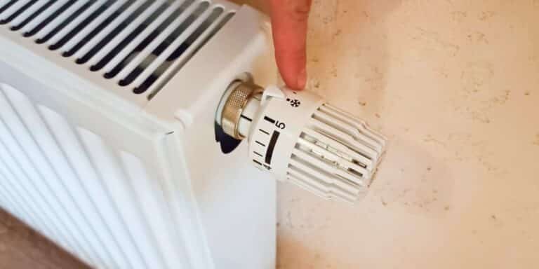 Doigt ajustant un thermostat de radiateur blanc.
