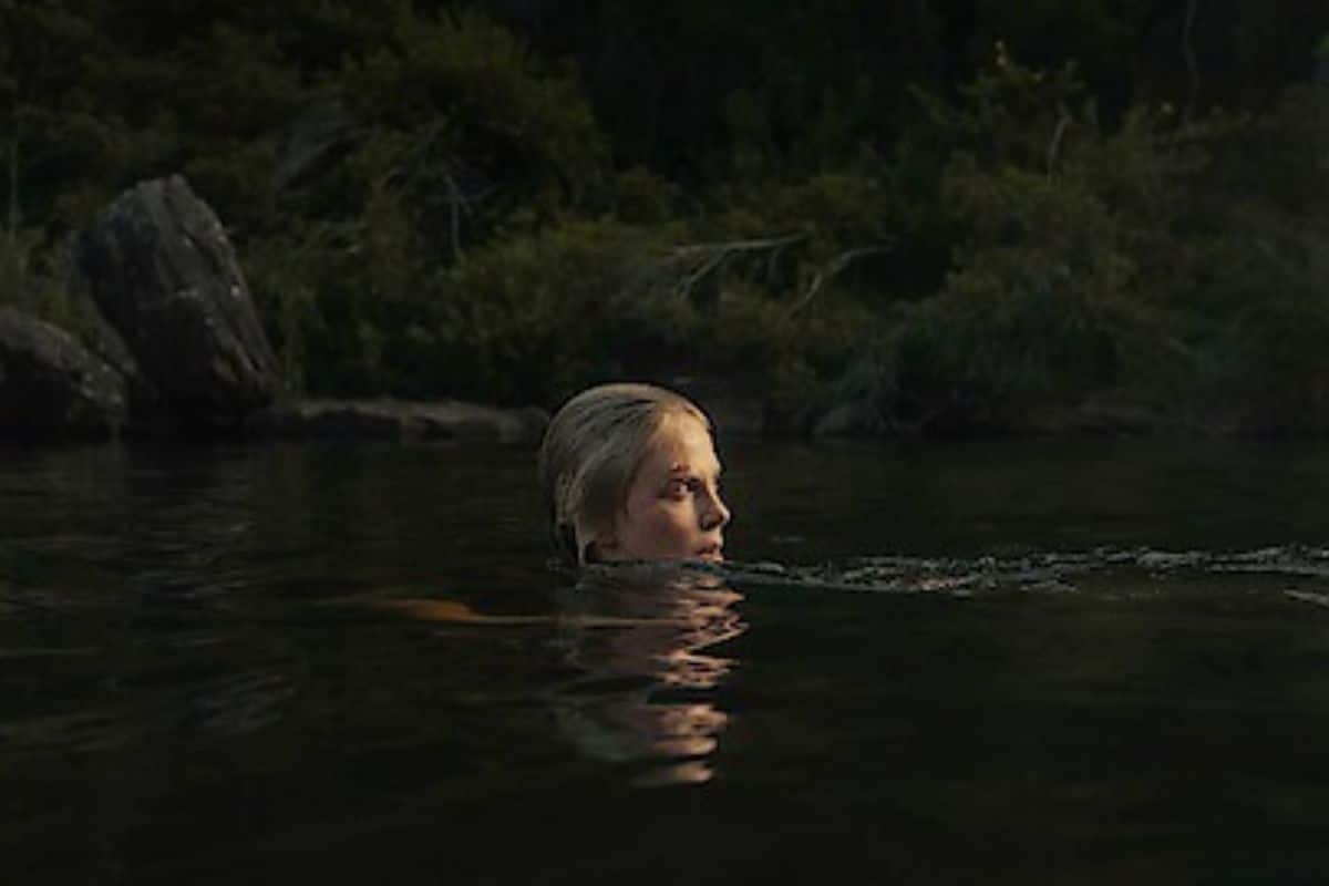 Femme nageant dans un lac, entourée de nature.