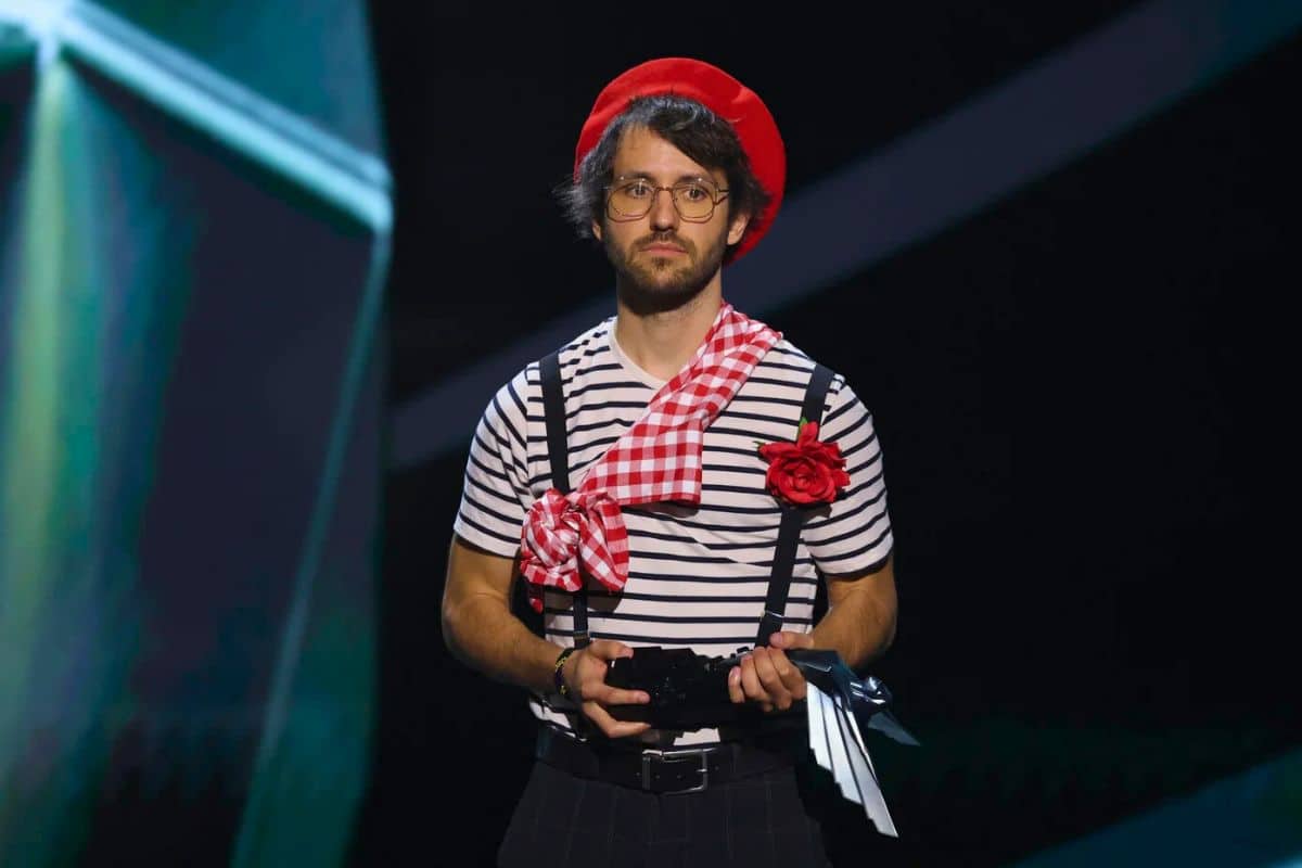 Homme avec béret rouge et chemise rayée.
