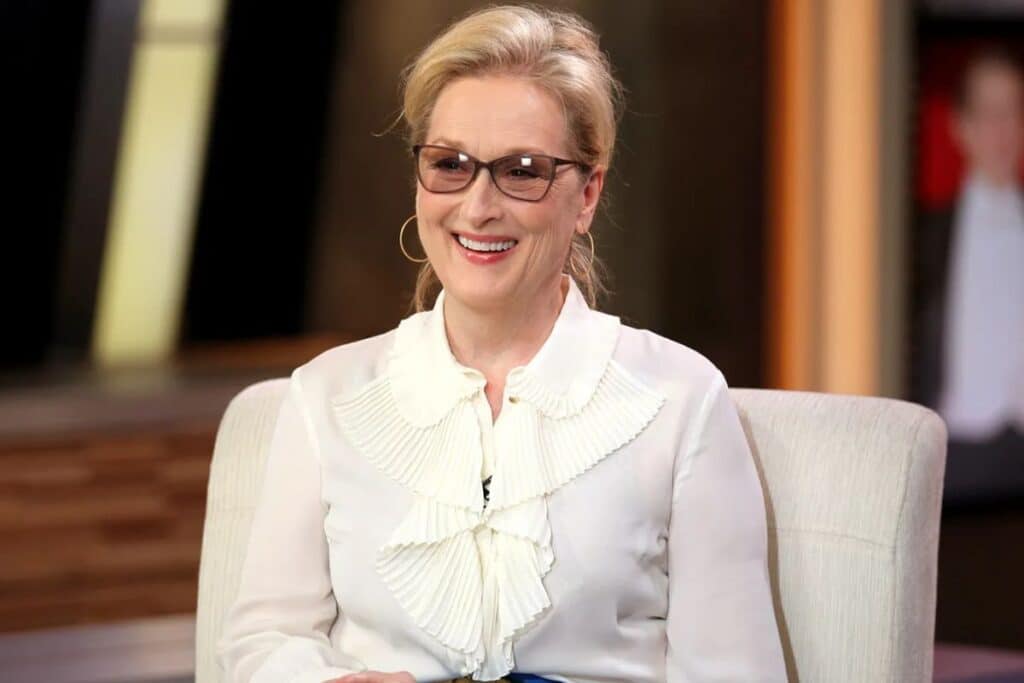 Femme souriante en chemisier blanc, lunettes noires.