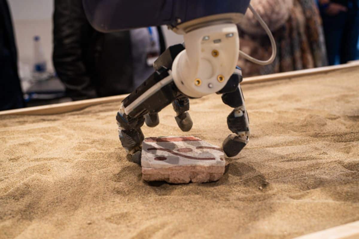 Robot ramassant une brique sur le sable.