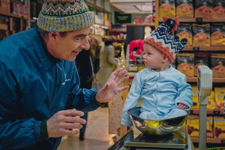Bébé pesé sur balance, homme souriant.