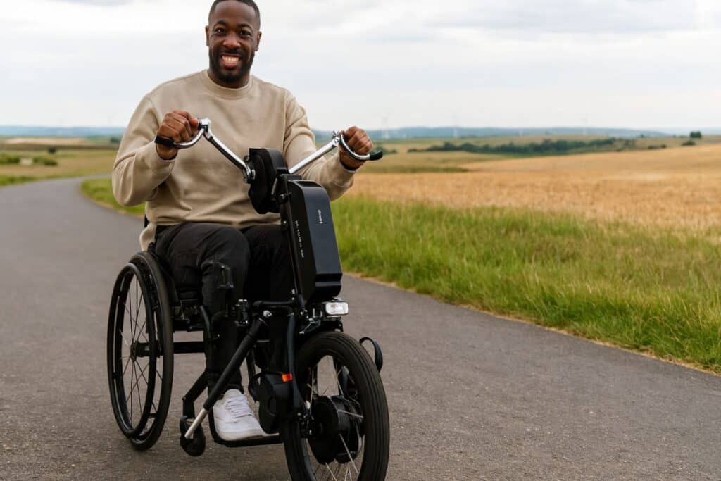 Homme souriant en fauteuil roulant sur une route campagne.