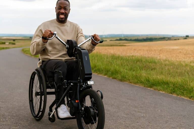 Homme souriant en fauteuil roulant sur une route campagne.