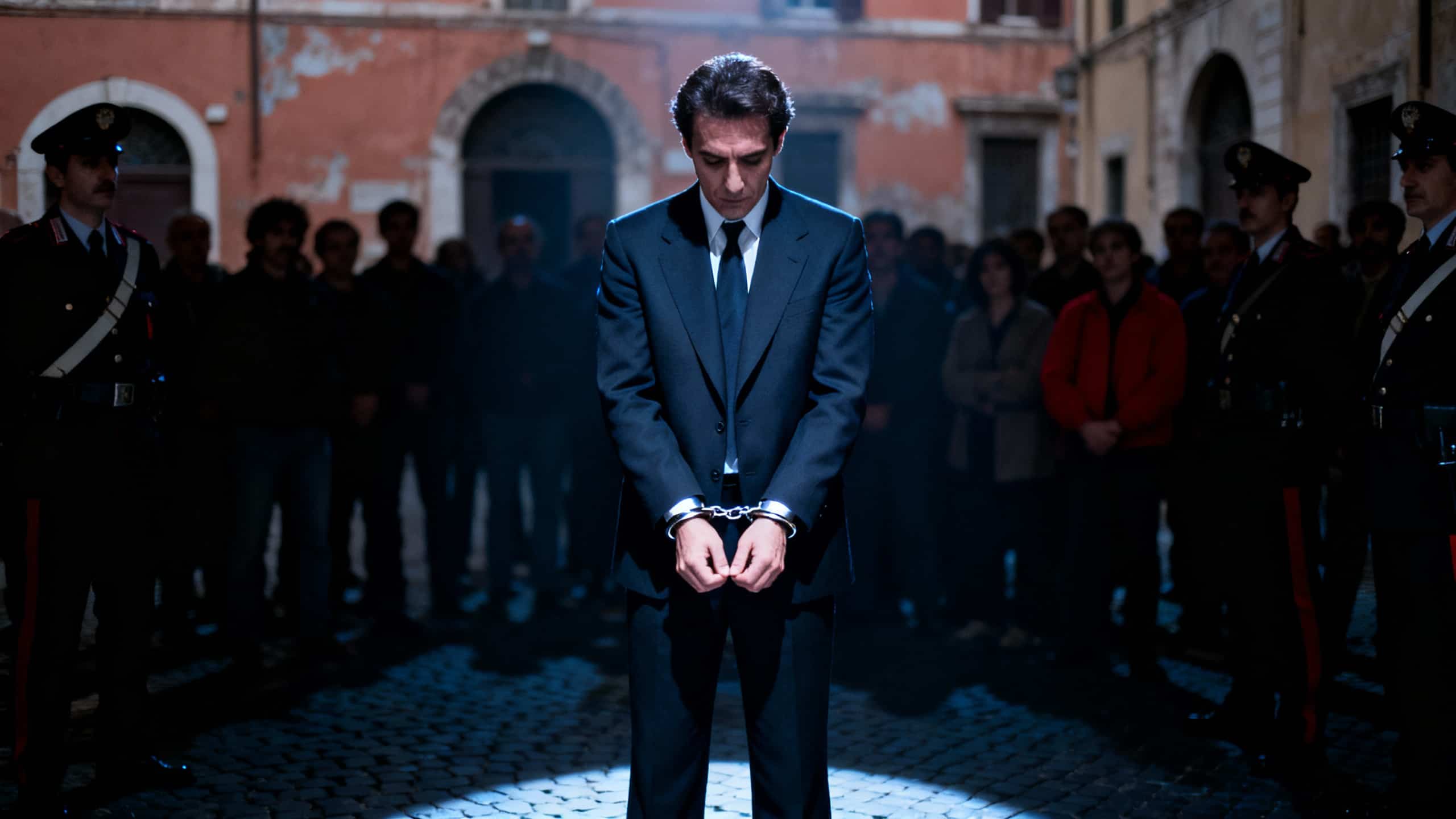 Homme menotté entouré de policiers et de foule.