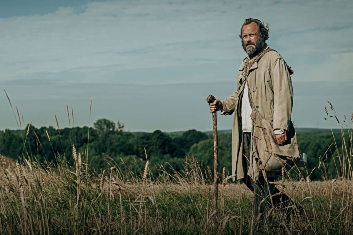 Homme marchant dans un champ avec bâton.