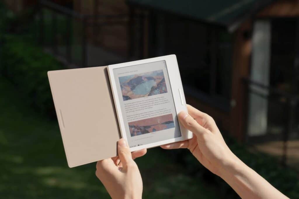 Personne tenant une liseuse ouverte en extérieur.