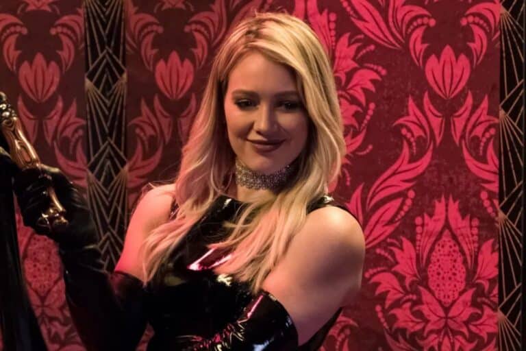 Personne blonde souriante devant fond rouge décoratif.