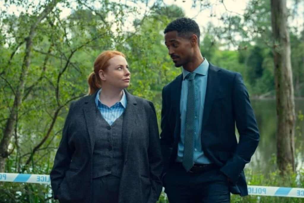 Deux enquêteurs discutent près d'une rivière en forêt.