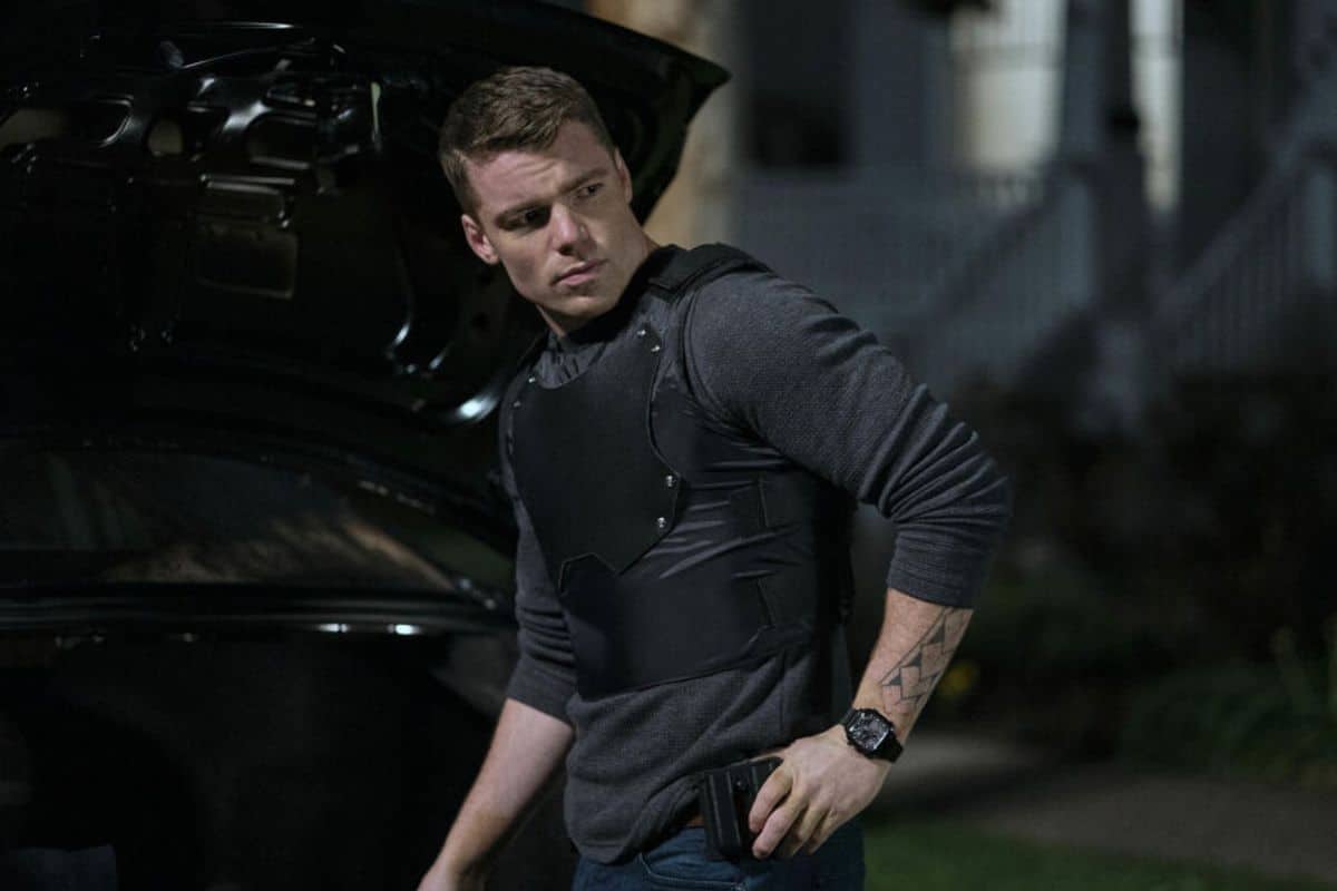 Homme en gilet pare-balles près d'une voiture.