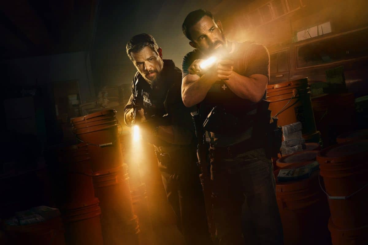 Deux hommes armés dans un entrepôt sombre.