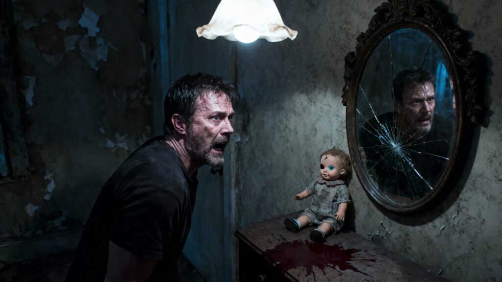 Homme effrayé face à une poupée et un miroir.