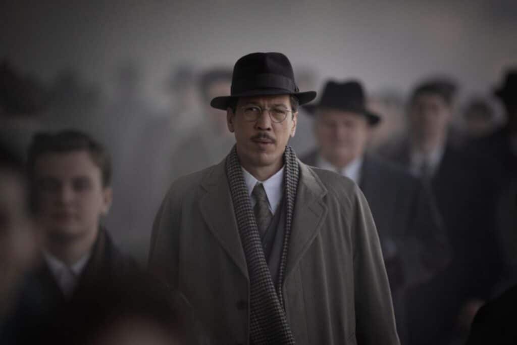 Homme en manteau et chapeau parmi la foule.