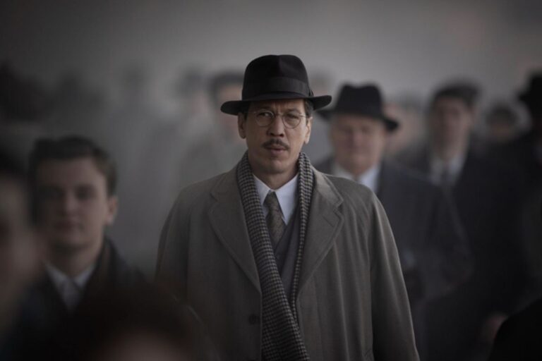 Homme en manteau et chapeau parmi la foule.