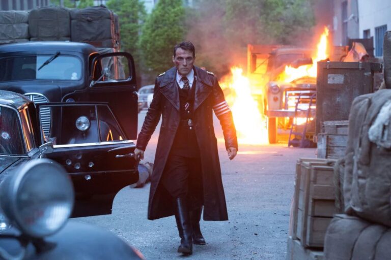 Homme en manteau sombre près d'une voiture et feu.