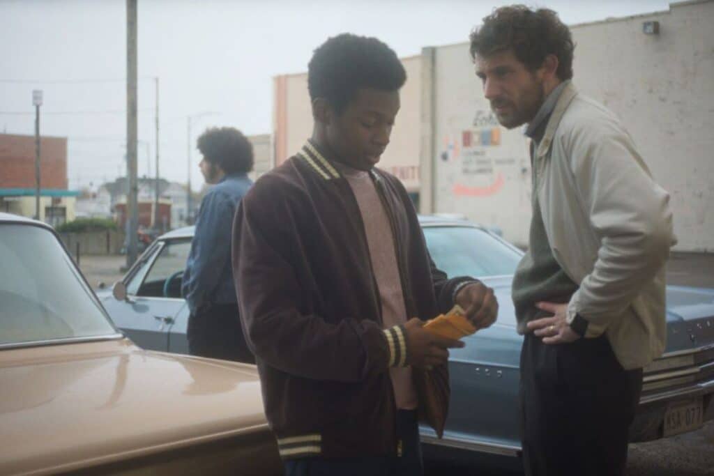 Deux hommes discutent devant des voitures dans la rue.