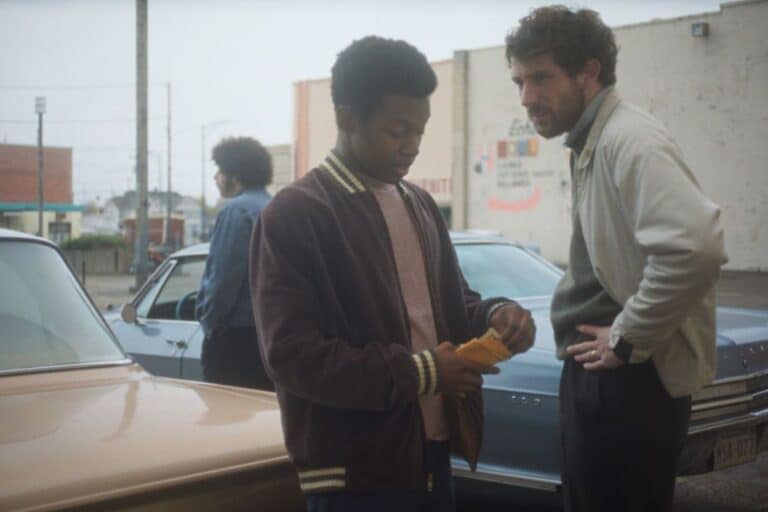 Deux hommes discutent devant des voitures dans la rue.