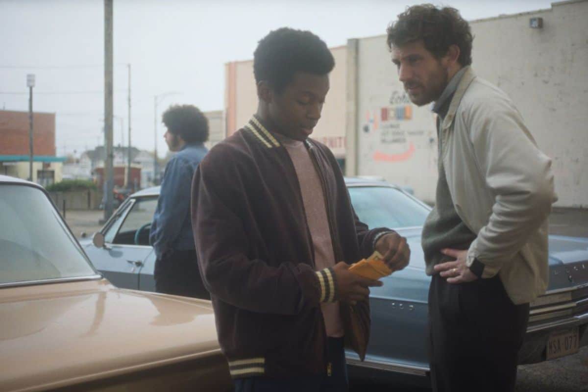 Deux hommes discutent devant des voitures dans la rue.