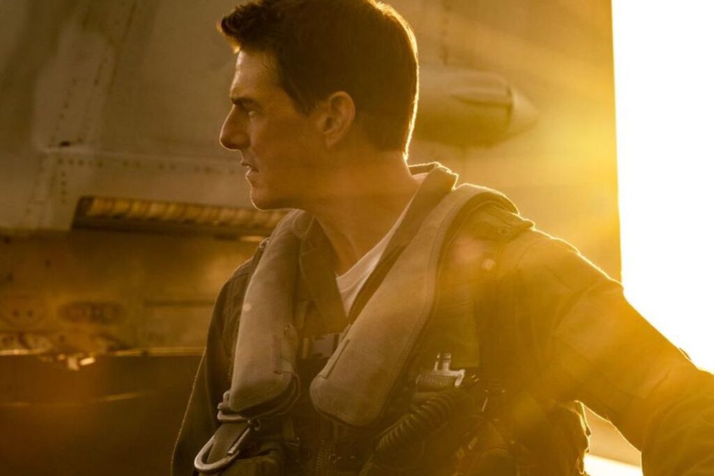 Homme en uniforme devant avion au coucher du soleil.