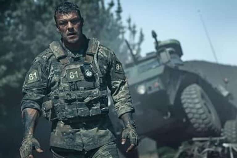 Soldat en treillis militaire devant un véhicule blindé.