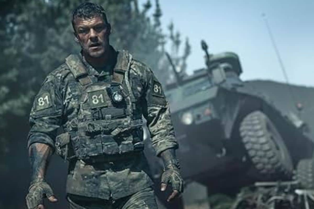 Soldat en treillis militaire devant un véhicule blindé.